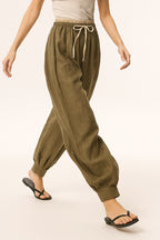Model bending forward in peach linen tapered trousers, movement detail