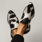 Black and white cow print pointed toe loafer shown from the side