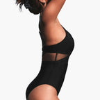 Model wearing black mesh insert swimsuit, side profile pose