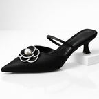 Close-up of white pearl-centred flower detail on black leather mule