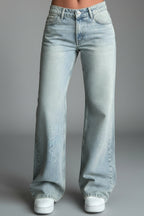 Model wearing light blue low waist jeans with white top, standing pose
