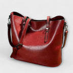 Woman holding tan leather tote with both handles, standing pose